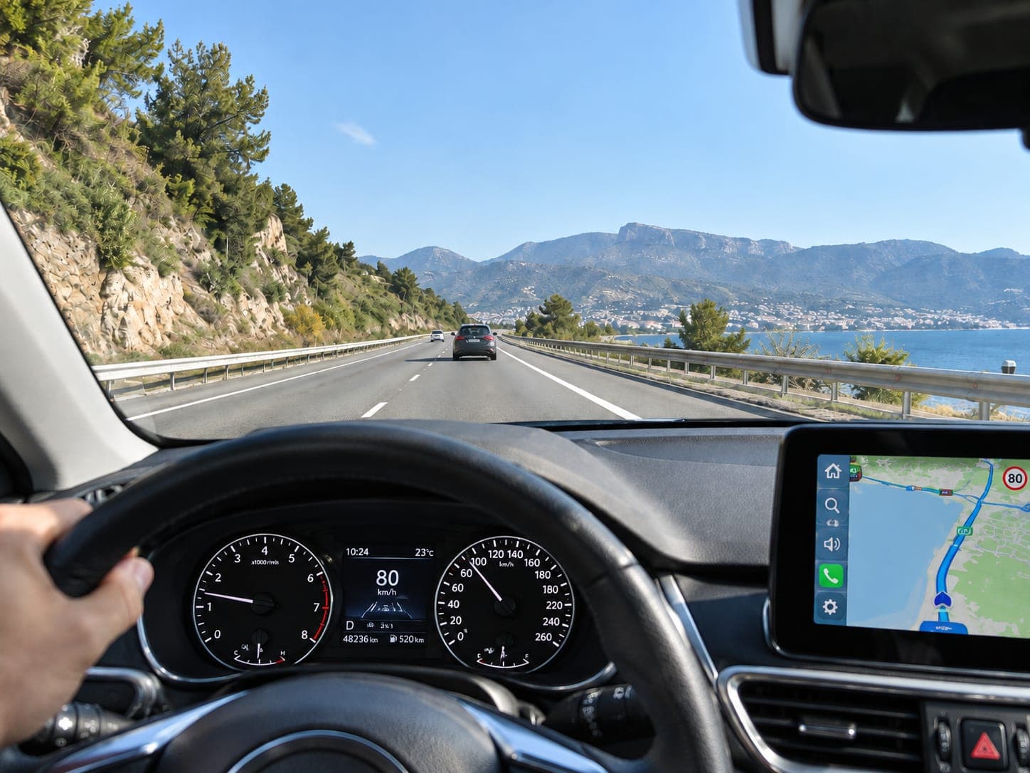 Vista desde el asiento del conductor en una carretera de costa: la carretera, el salpicadero y la pantalla del coche se ven nítidos
